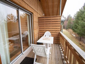 Eine Holzterrasse mit Tisch und Stühlen, eine Glastür und Blick auf Bäume.