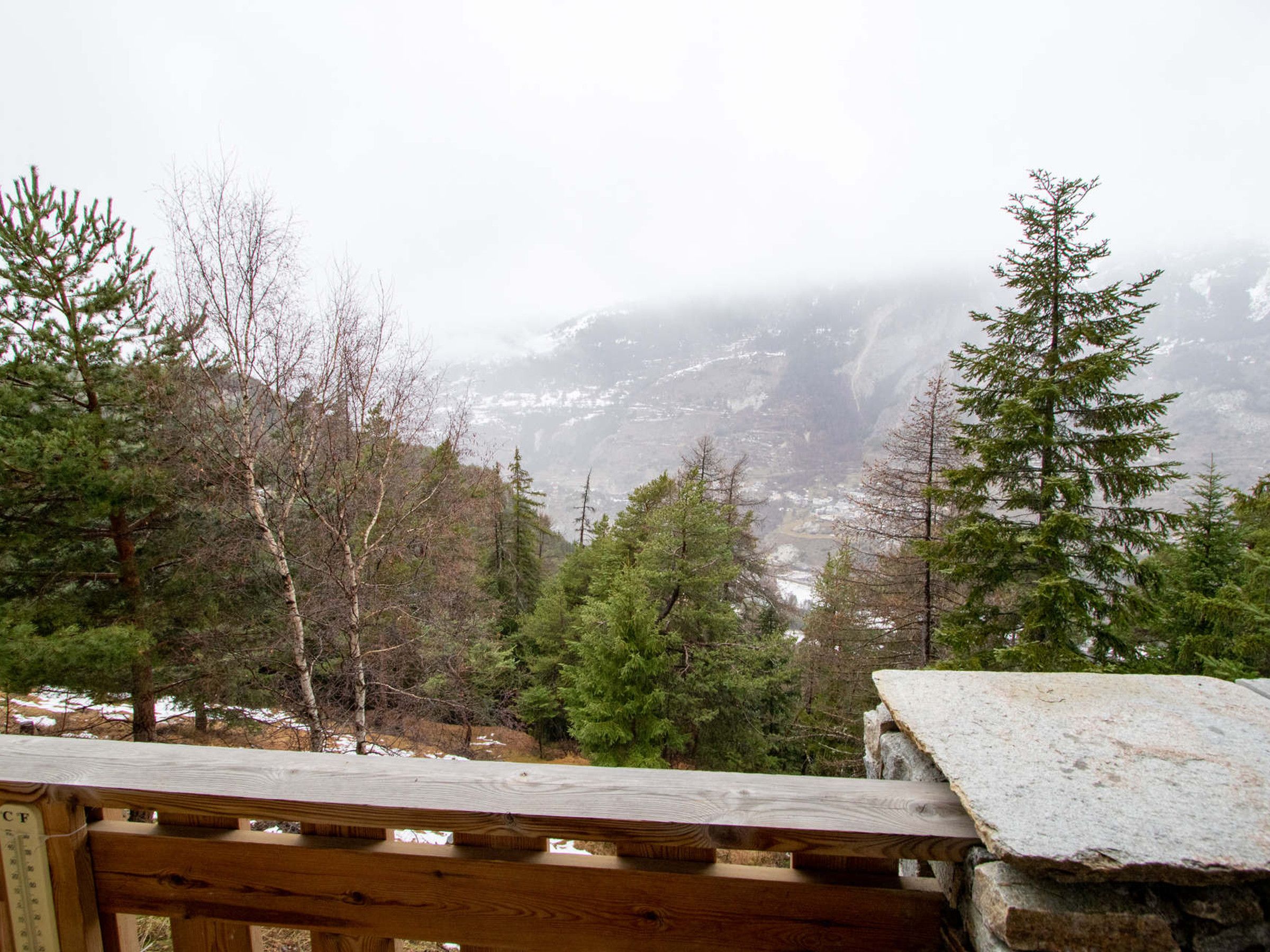 Un patio in legno con un davanzale in pietra, che si affaccia su una valle boscosa con montagne sullo sfondo.
