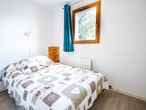 A bedroom with a bed, a window with a curtain, a radiator, and a wooden shelf. - Spacious apartment, park view - 10 guests (Valfréjus)
