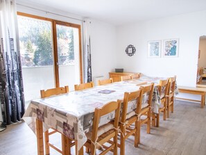 A dining area with a long table and chairs, a clock on the wall, and a window with curtains. - Spacious apartment, park view - 10 guests (Valfréjus)