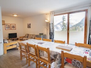 A cozy room with a dining table, chairs, a sofa, a television, and a window with a mountain view. - Spacious apartment, park view - 10 guests (Valfréjus)