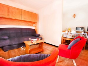 A living room with a sofa, a red chair, a wooden coffee table with glasses and cups, and a kitchenette with a microwave and coffee maker. - Apartment pets welcome - 4 guests piste view (Villarodin-Bourget)