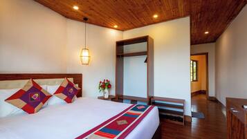 A hotel room with a large bed, a wooden ceiling, a nightstand with a vase of flowers, and a mirror.