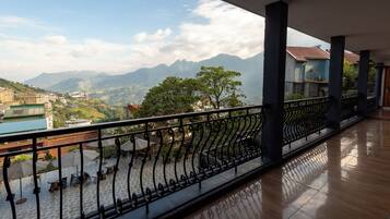 A balcony with a metal railing overlooking a mountainous landscape with buildings in the distance.