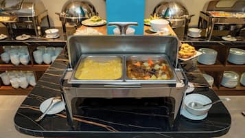 A buffet setup with two serving dishes, one containing a yellow dish and the other a stew with vegetables.