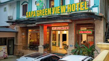 The exterior of Sapa Green View Hotel with a signboard, entrance, and two cars parked in front.