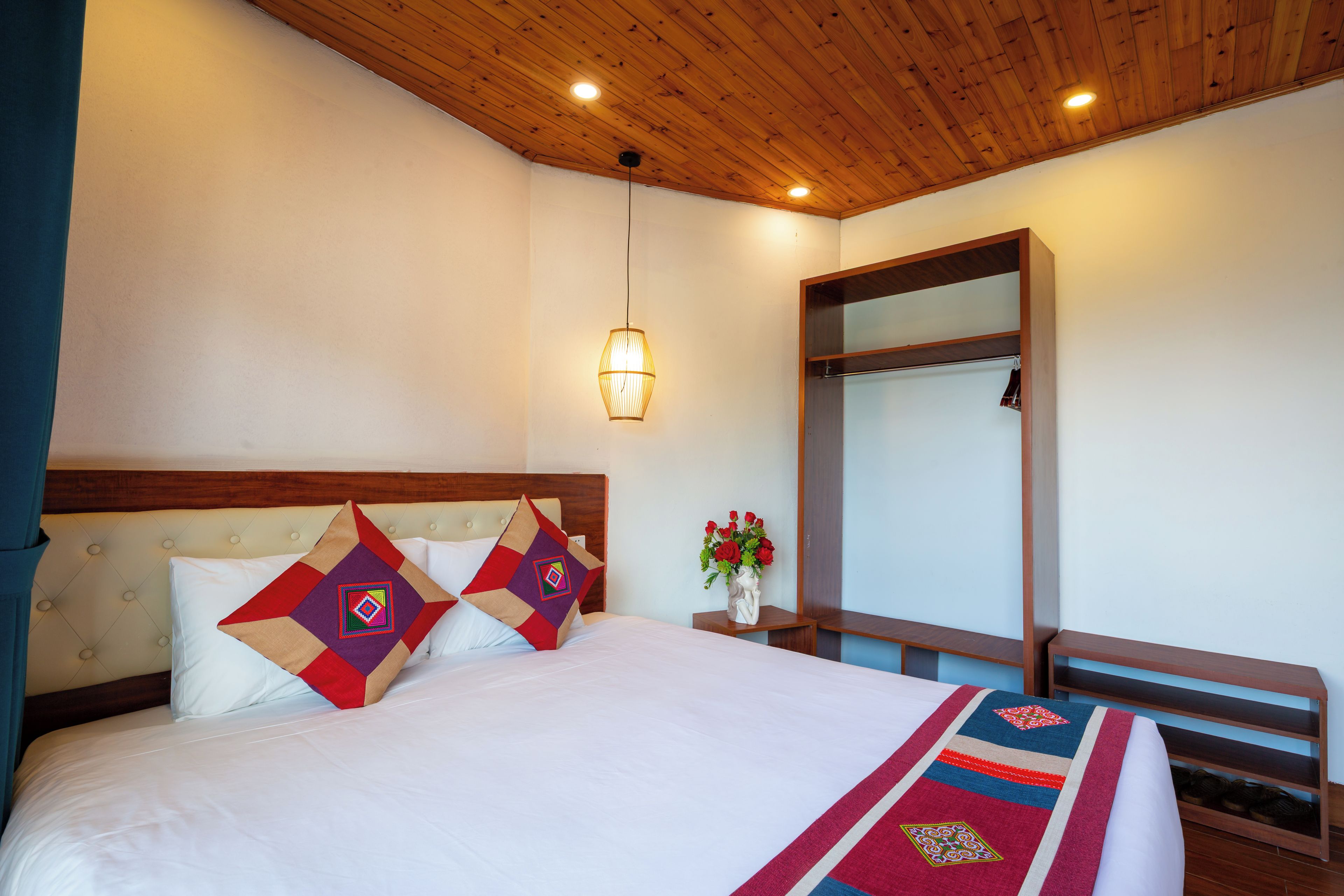 Habitación de hotel con cama, mesita de noche, espejo y lámpara colgante.