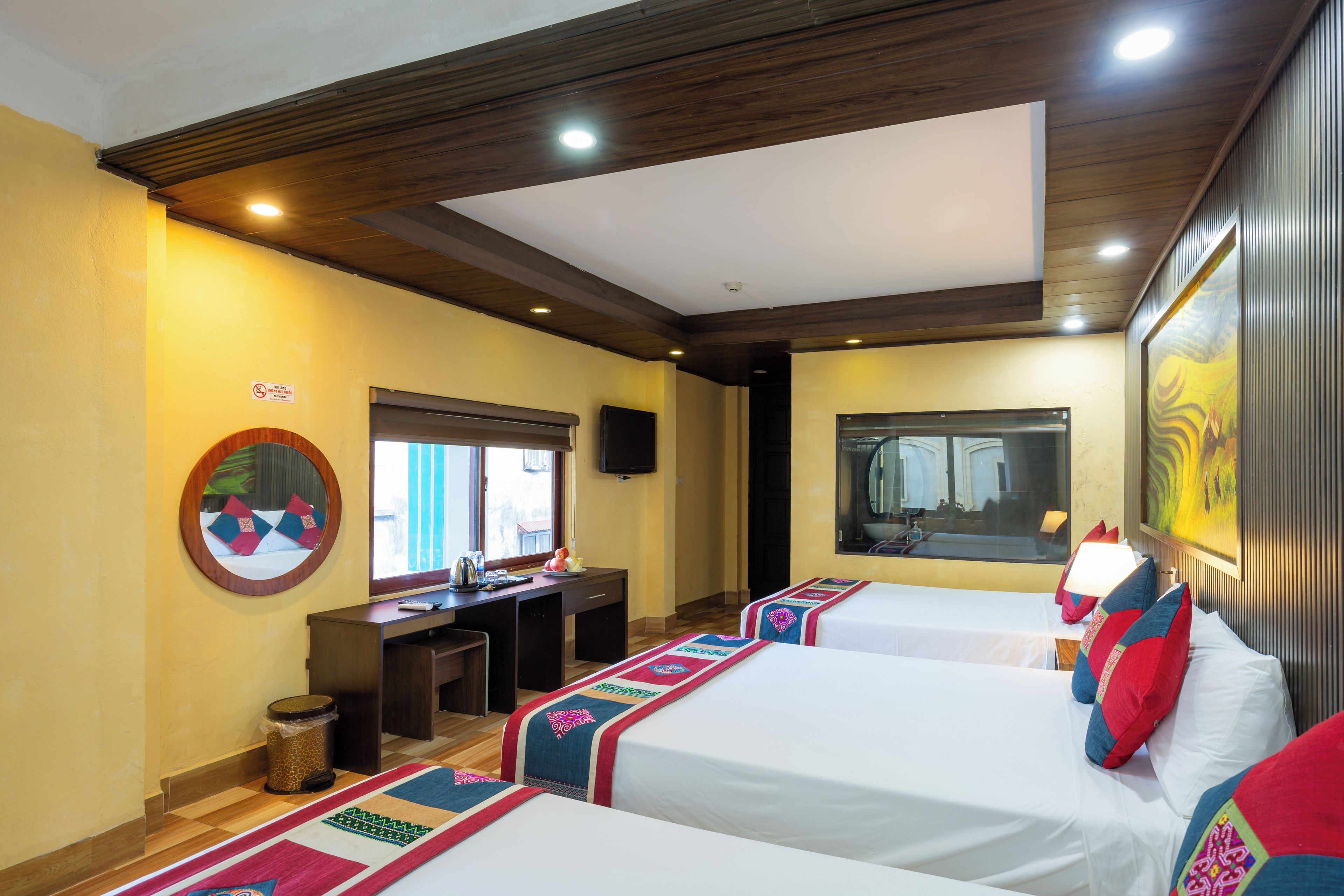 A hotel room with two beds, a desk, a trash can, and a large window.