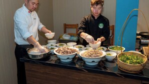 Two individuals preparing food in a kitchen with various bowls of ingredients and a stove. - Green View Hotel Sapa (Sa Pa)