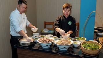 Dos personas preparando comida en una cocina con varios recipientes de ingredientes y una estufa.