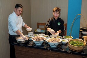Two individuals preparing food in a kitchen with various bowls of ingredients and a stove. - Green View Hotel Sapa (Sa Pa)
