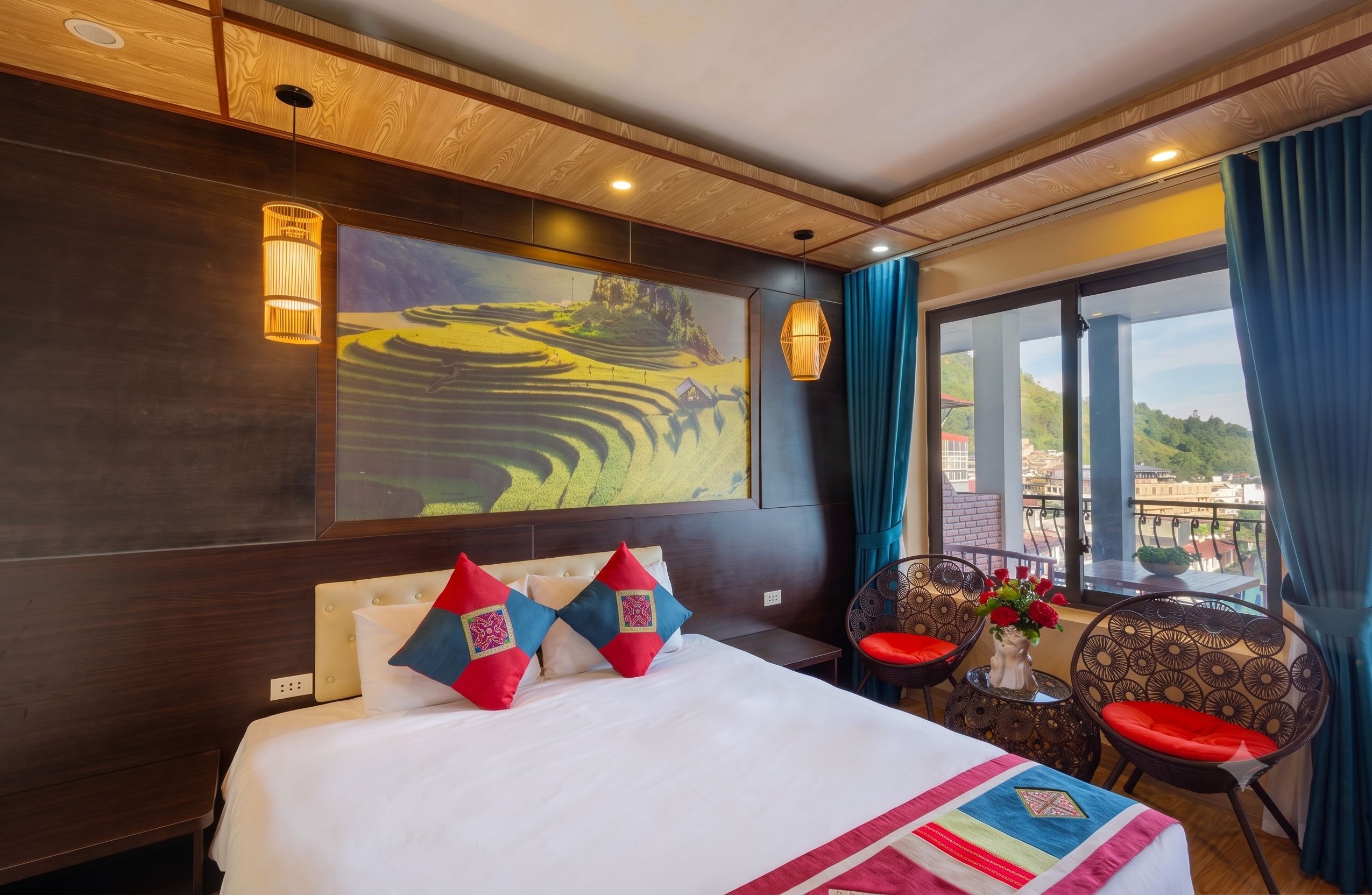 Habitación de hotel con una cama grande, dos almohadas decorativas, un cuadro en la pared, una mesita con un florero y vistas al exterior a través de una ventana.