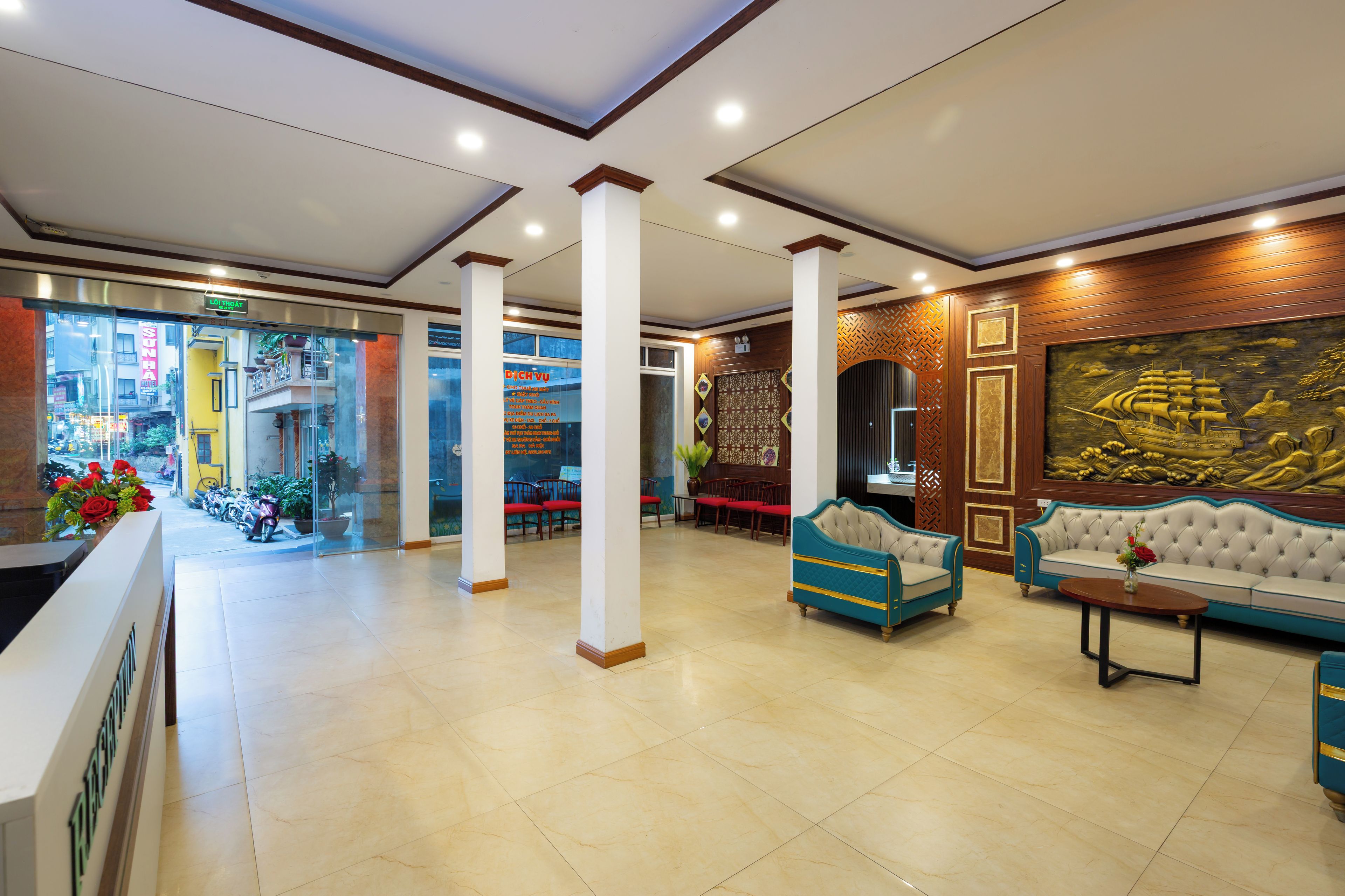 Vestíbulo de hotel con mostrador de recepción, zona de estar con sofás y sillones, un mural grande y vista a la calle.