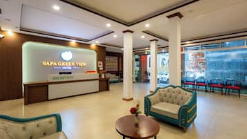 A hotel reception area with a reception desk, seating, and a view of the street.