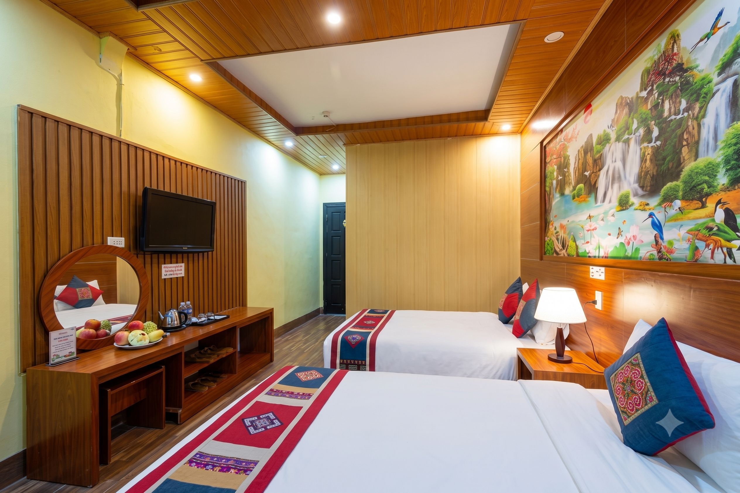 A hotel room with two beds, a TV, a desk with a mirror, and a painting of a waterfall.