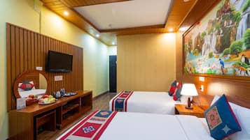 A hotel room with two beds, a TV, a desk with a mirror, and a painting of a waterfall.