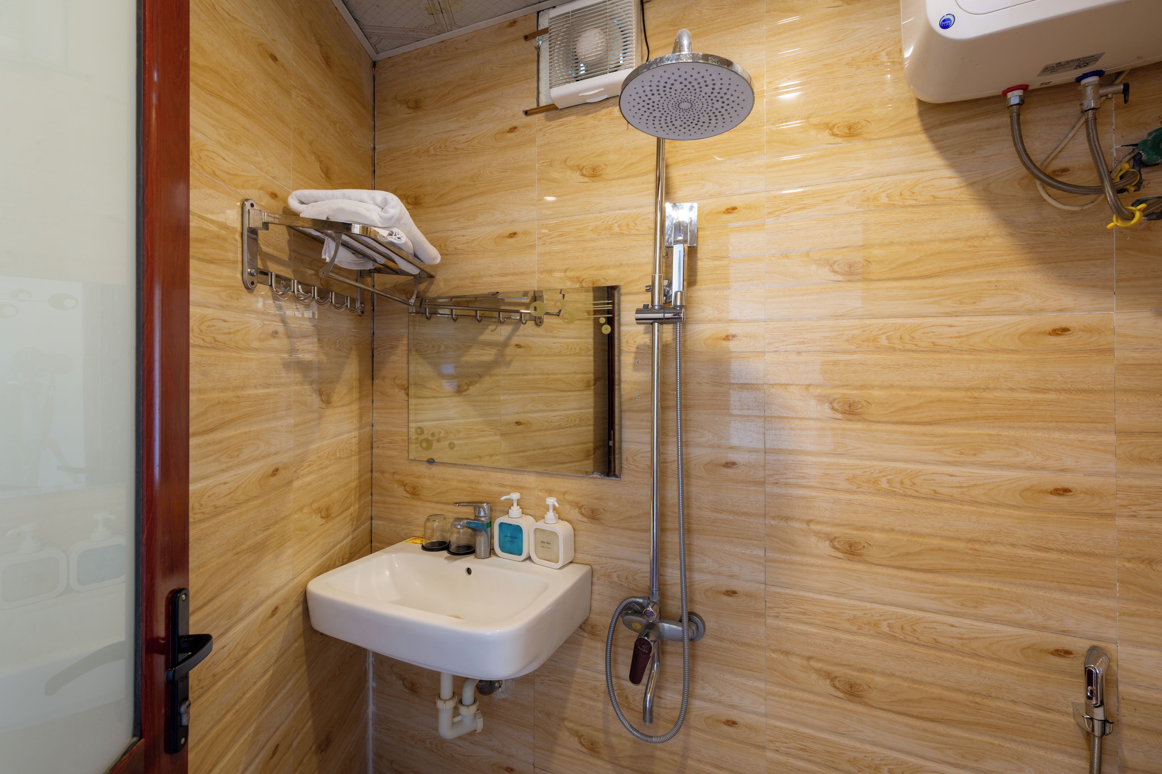 A wooden-paneled bathroom with a sink, hand soap, and a handheld showerhead.
