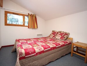A bedroom with a bed, a window with curtains, a bedside table, and a radiator. - Duplex in Valfréjus center - 10 guests near slopes (Valfréjus)