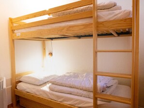 Ein Etagenbett mit Holzrahmen, weißer Bettwäsche und einer an der Wand montierten Lampe.