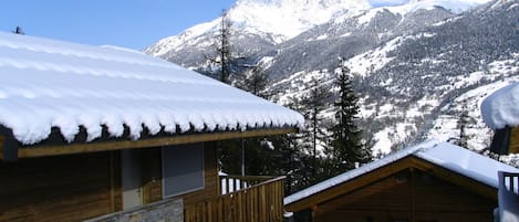 Een houten chalet met een balkon, omgeven door besneeuwde bergen en bomen.