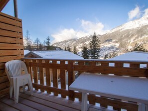 Eine Holzdiele mit einem weißen Plastikstuhl und einem Tisch, mit Blick auf eine verschneite Berglandschaft.