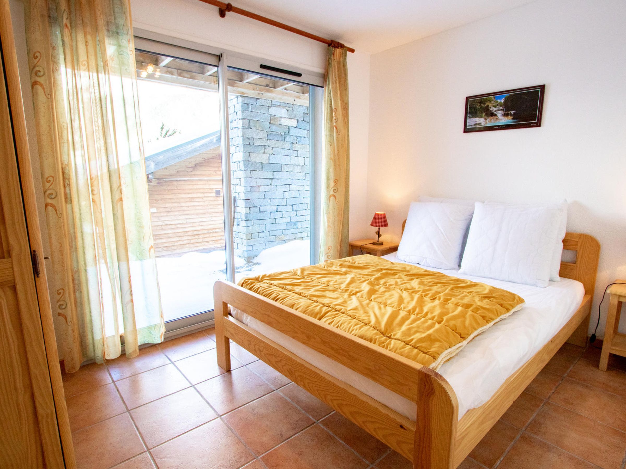 Una camera da letto con un letto, un comodino, una lampada, una finestra con tende e un quadro appeso al muro.