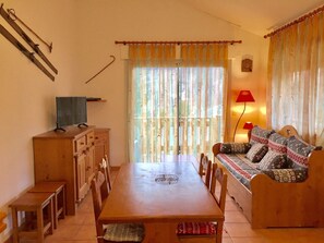 Ein Essbereich mit einem Holztisch, Stühlen, einer Couch und einem Fernseher auf einem Schrank.