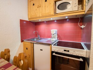 Eine kompakte Küche mit Mikrowelle, Kaffeemaschine, Spüle und Backofen.
