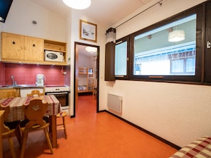 Eine kompakte Küche mit Mikrowelle, Herd und Spüle, ein Essbereich mit Tisch und Stühlen sowie ein Fenster mit Außenblick.