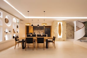 Ein moderner Essbereich mit Holztisch und -stühlen, Pendelleuchten und einer Küche im Hintergrund.