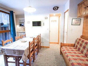 Ein kompakter Wohnraum mit Essbereich, einer Küchenzeile, einer Couch und einer Tür zu einem weiteren Zimmer.
