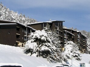 Ein mit Schnee bedecktes Gebäude mit mehreren Balkonen, umgeben von Bäumen.