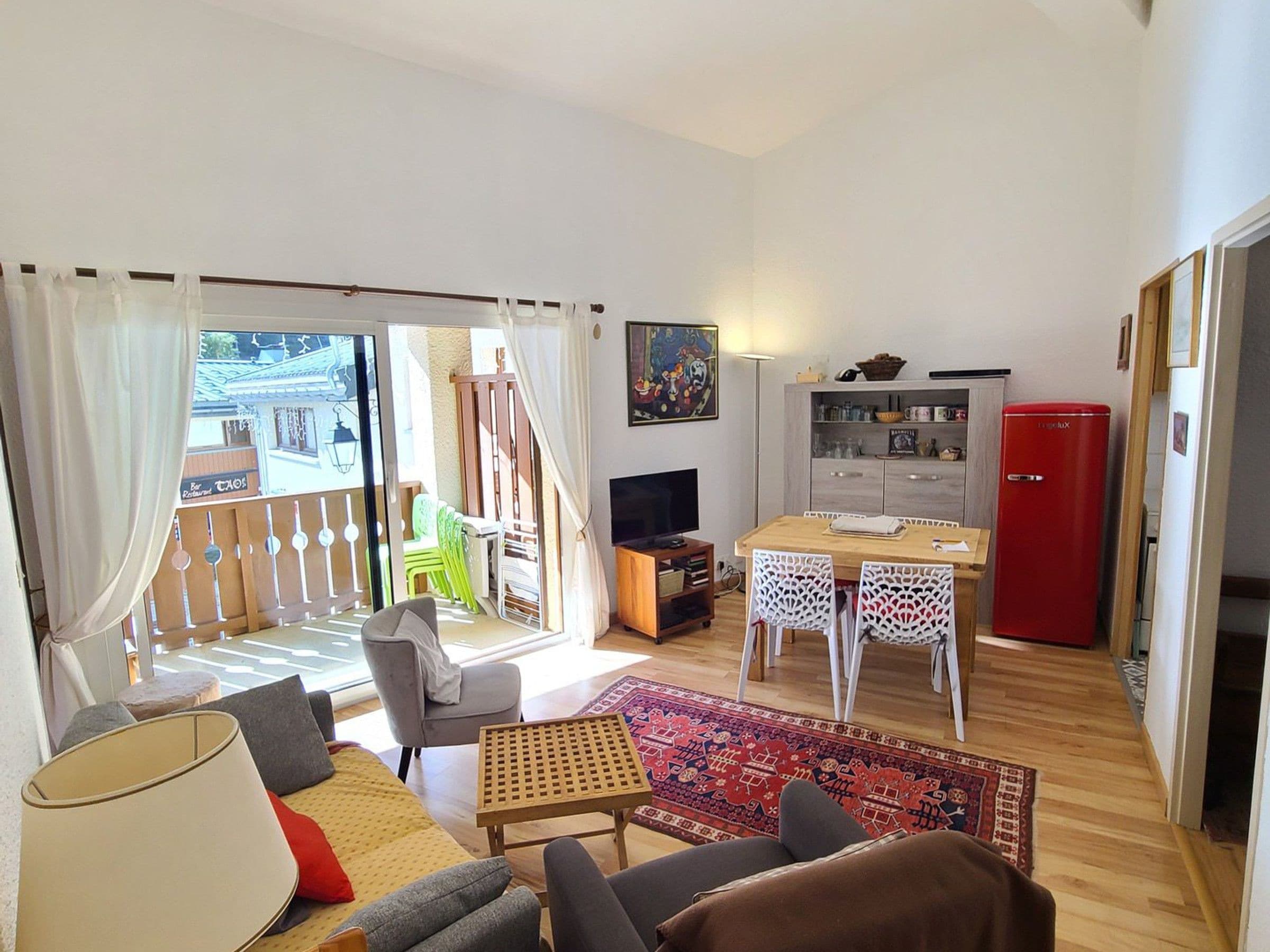A living room with a sofa, a TV, a dining table, and a red refrigerator.