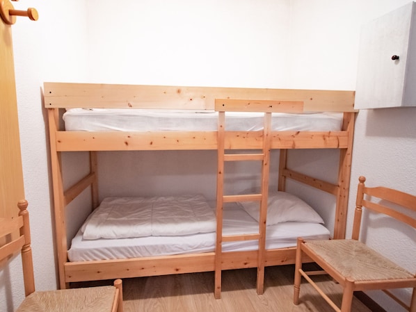 Ein Stockbett mit einer Leiter, ein Holzstuhl und eine weiße Wand.
