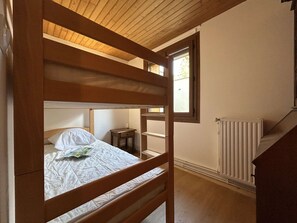 Ein Schlafraum mit Etagenbett, einem hölzernen Kopfteil, einem kleinen Nachttisch und einem Heizkörper an der Wand.