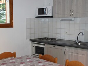Eine Küche mit Mikrowelle, Herd, Backofen und Spüle. Ein Tisch mit Stühlen und ein Fenster sind vorhanden.
