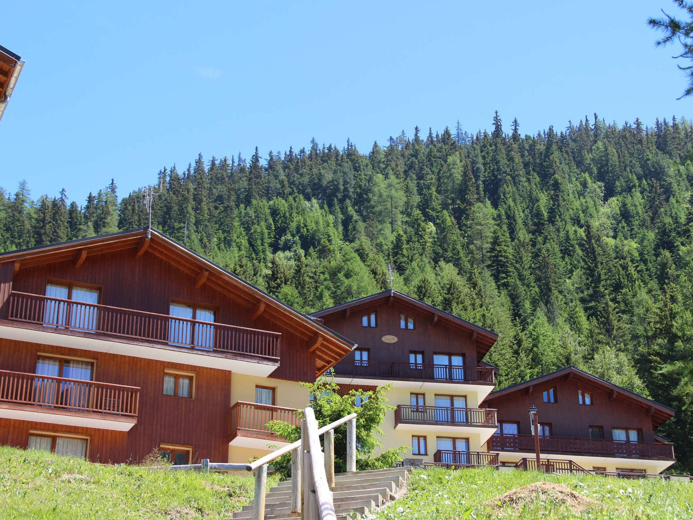 A wooden chalet with balconies, set against a forested hillside.