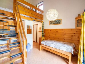 A room with a wooden staircase, a bed with a patterned bedspread, a hanging light fixture, and a window with curtains. - Spacious apartment at the foot of the slopes - 8 guests (Villarodin-Bourget)