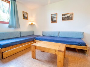 A cozy room with a wooden bench, a small table, and two blue-patterned sofas. - Spacious apartment at the foot of the slopes - 8 guests (Villarodin-Bourget)