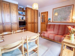 A cozy living room with a wooden dining table, chairs, a sofa, and a television. - Apartment with balcony, mountain view - 6 guests (Villarodin-Bourget)