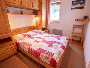 A bedroom with a wooden bed, a nightstand, a chair, a shelf with decorative items, and a window with a view of a snowy landscape. - Apartment with balcony, mountain view - 6 guests (Villarodin-Bourget)