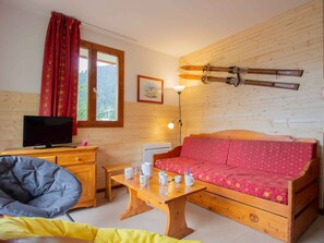 Ein gemütliches Zimmer mit einem hölzernen Bett, einem Fernseher, einem Schreibtisch mit Stuhl und einem Fenster mit Vorhängen.
