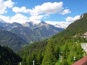 A mountain landscape with a clear sky, a valley, and a building with a sloped roof. - Studio for 4, station and Vanoise view (Valfréjus)