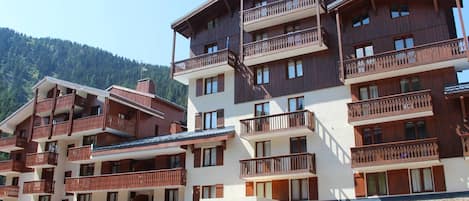 Een hotel met meerdere verdiepingen, voorzien van balkons, een restaurant genaamd 'CREPERIE SPECIALITES SAVOYARDES', en een bord met de tekst 'LOCATION DE SKIS'.