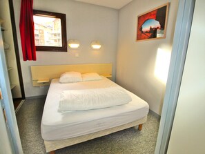 Hotellihuone, jossa on sänky, kaksi yöpöytälamppua, ikkuna, jossa on verhot, ja taulu seinällä.
