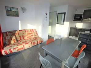 A compact living space with a sofa, dining table, chairs, a kitchen area with a microwave, and a painting on the wall. - Apartment pets OK - 6 guests (village view) (Villarodin-Bourget)