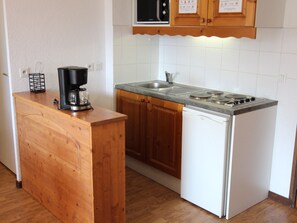A compact kitchen with wooden cabinets, a built-in stove, and a coffee maker on a wooden counter. - Apartment mountain view - 6 guests (Villarodin-Bourget)
