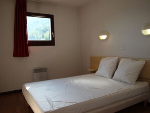 A single-bed room with a window, a wall-mounted heater, and a bedside table with a lamp. - Apartment mountain view - 6 guests (Villarodin-Bourget)