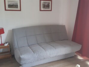 Ein graues Sofa in einem Zimmer mit einem Holznachttisch und einer roten Lampe.