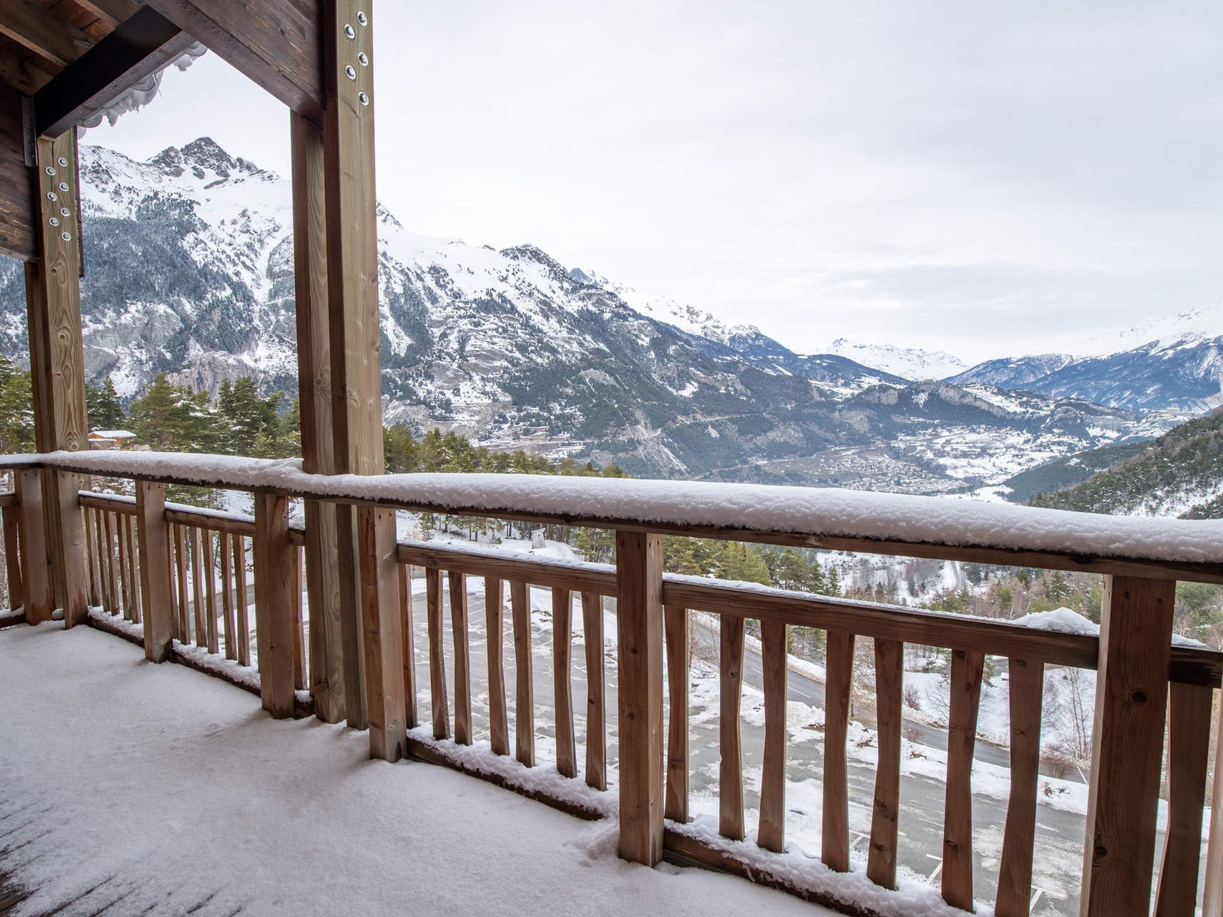 A wooden balcony with a snow-covered railing overlooking a mountainous landscape.